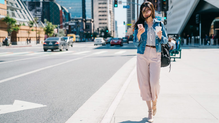 Challenger Banks - Asian woman a smart phone in the street on a sunny day holding a coffee
