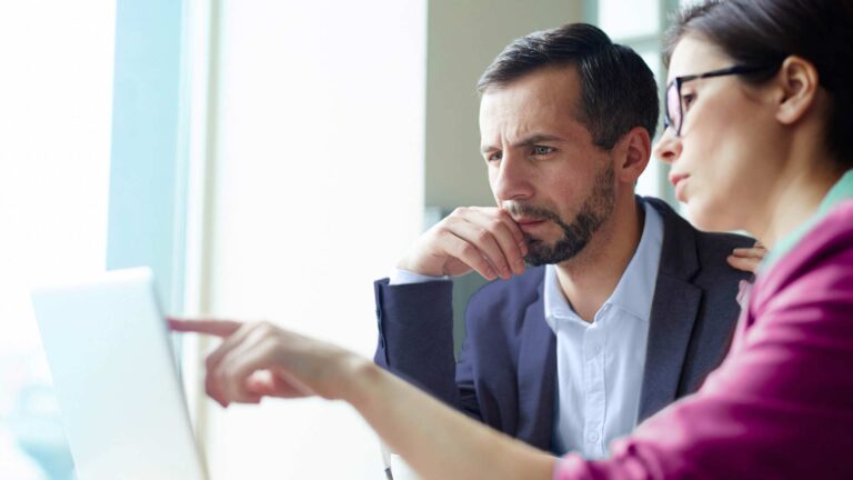 Man and woman at laptop. Woman is pointing to display and man is looking.