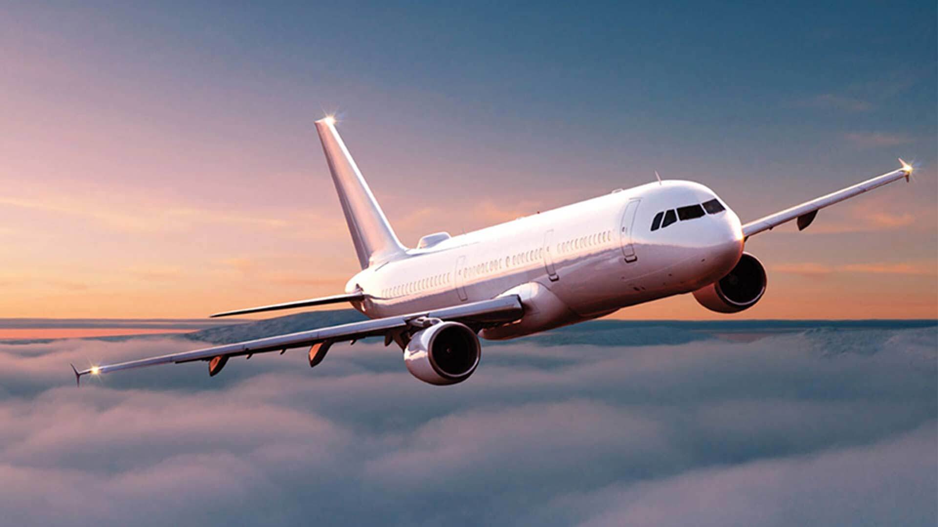 Airplane flying through the sky, a pastel-colored sunset and clouds can be seen in the background.