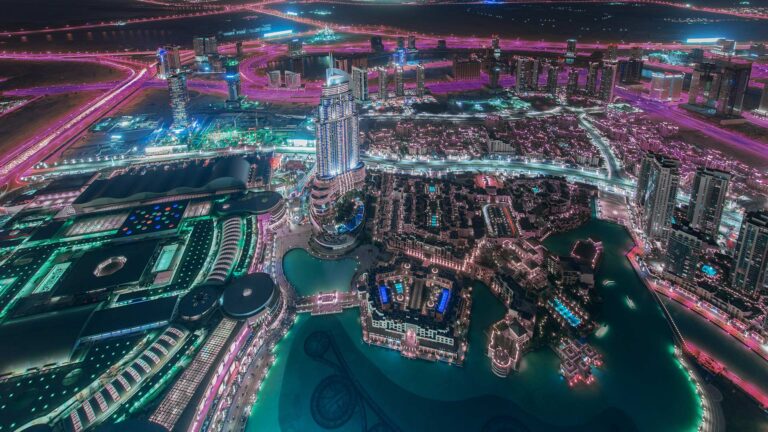 High level view of a city in the dark. Lights, details, and roads are illuminated with various blue and pink glows.