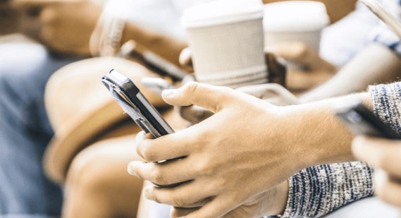 Close-up of several people's hands holding smartphones and disposable coffee cups. The scene conveys a sense of modern connectivity and casual socialization.