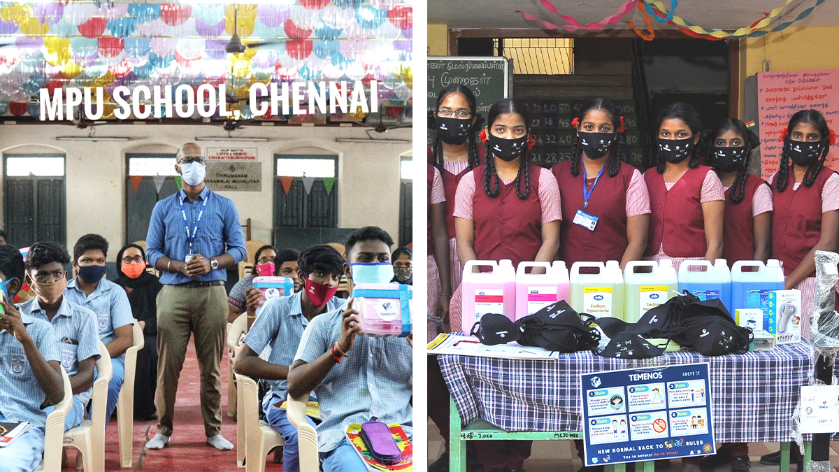 Students and a teacher at MPU School, Chennai, wear masks during an indoor event. Nearby, girls in uniform stand by a table with sanitizers and masks.