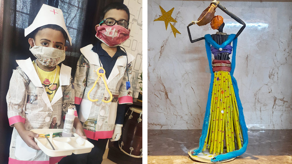 Two children stand in homemade healthcare costumes using newspaper and masks, holding medical props; beside them is a colorful tribal sculpture with a yellow skirt and blue scarf, set against a marble backdrop with a star decoration.   Try a different image