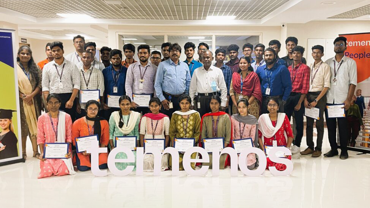 A group of young adults and two older men, all holding certificates, stand and kneel in rows in an office setting. A large "Temenos" sign is displayed in front. Everyone appears proud and accomplished.
