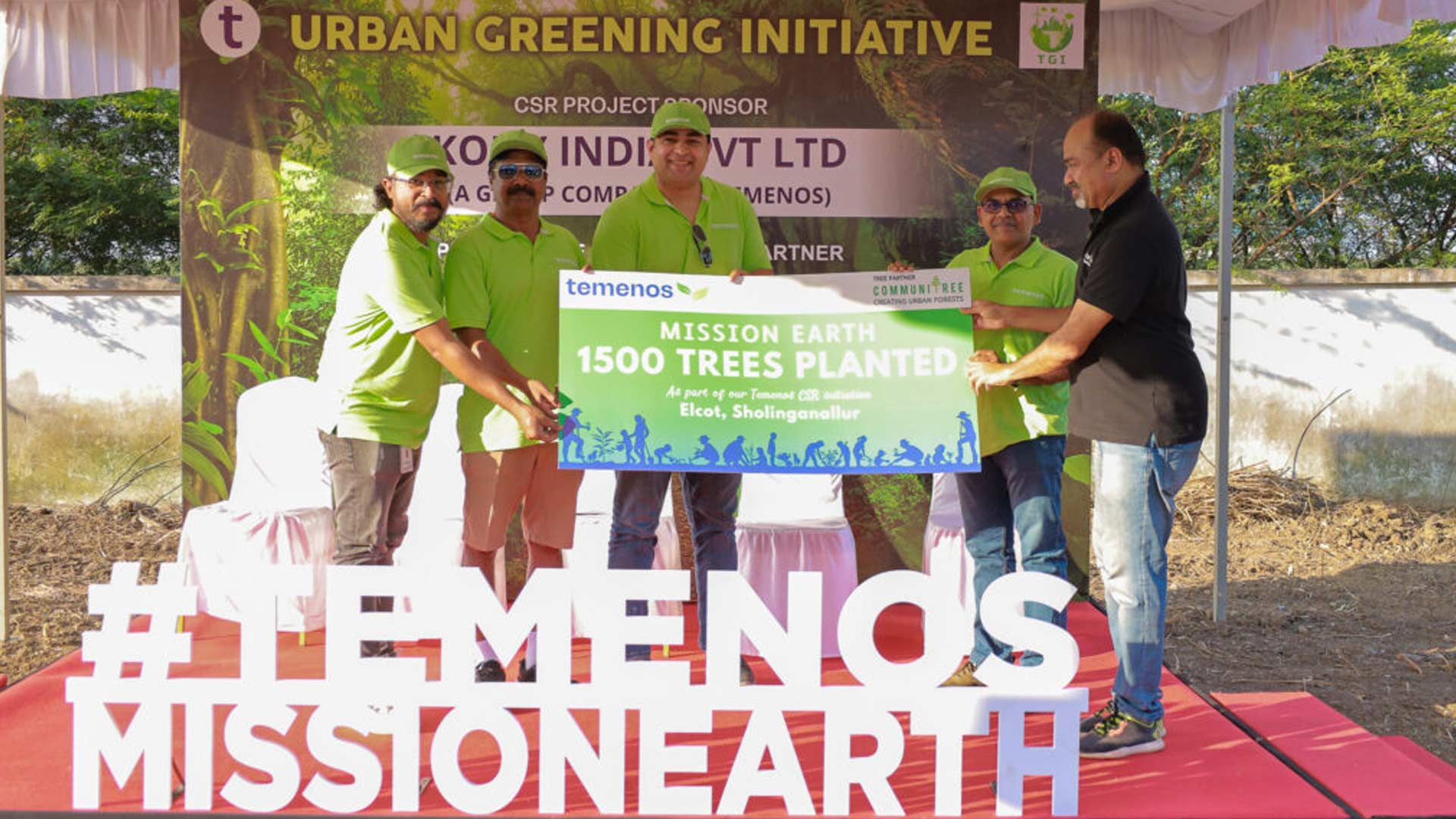 Five people hold a green sign saying “Mission Earth 1500 Trees Planted” at an outdoor event. They appear joyful, highlighting an urban greening initiative.