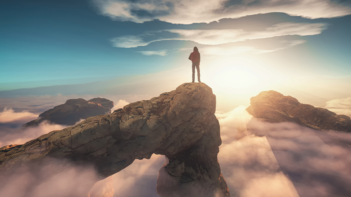 A person stands atop a rocky peak above clouds, facing a bright sunrise. The scene conveys a sense of adventure and awe. Blue sky and fluffy clouds surround.