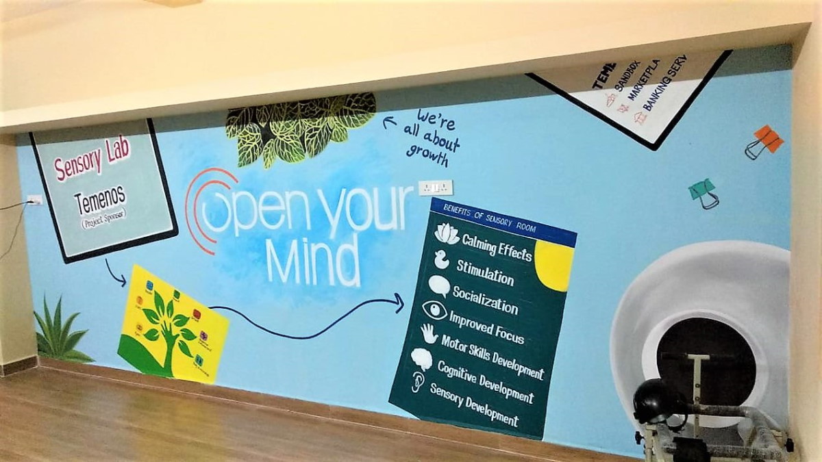 Colorful wall mural in a sensory lab featuring the text "Open Your Mind" with leaves, a diagram of benefits like calming and focus, and a stationary bike.