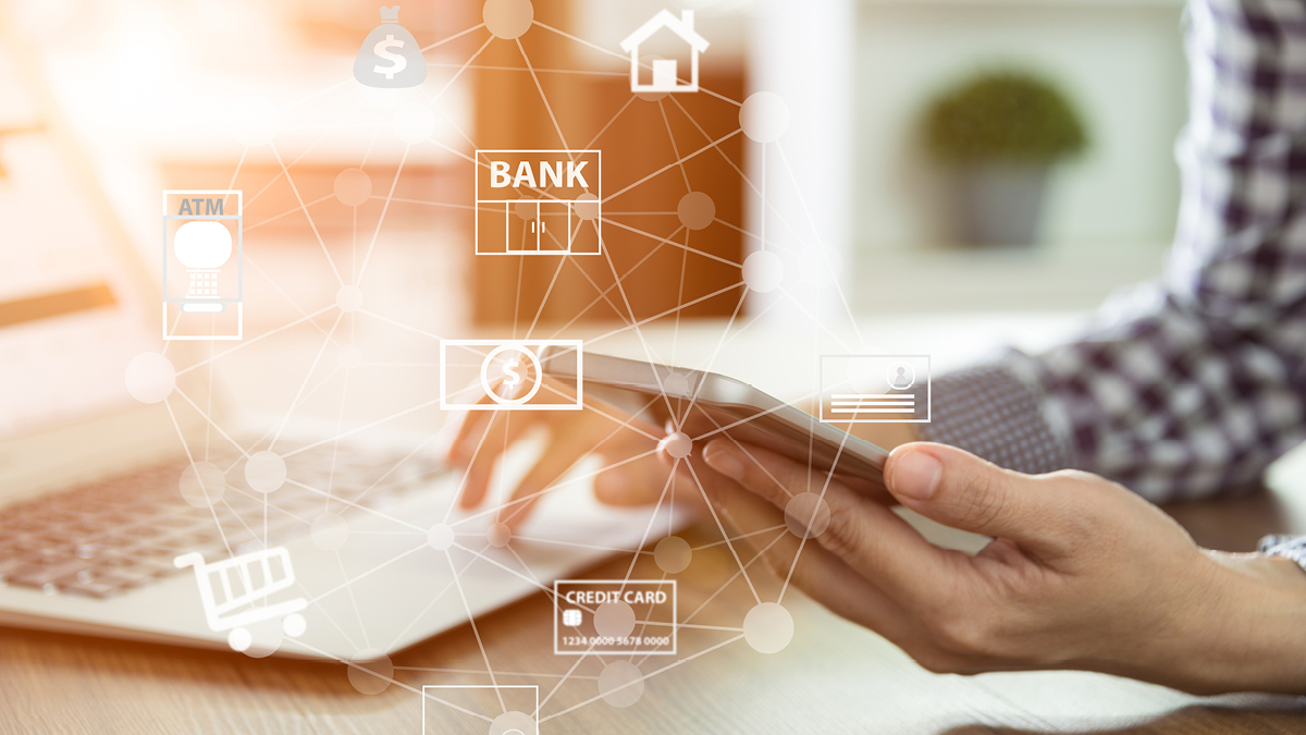 Man sitting at laptop looking at phone in hand