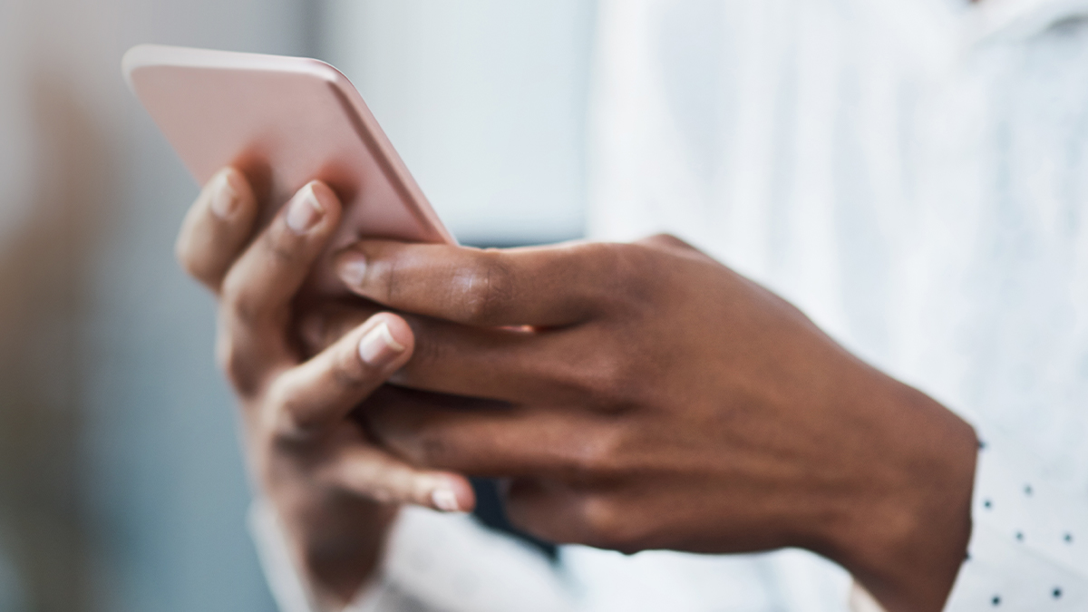 Close-up of a person holding a pink smartphone, focusing intently. Their fingers rest gently on the screen, with a blurred background suggesting a calm setting.