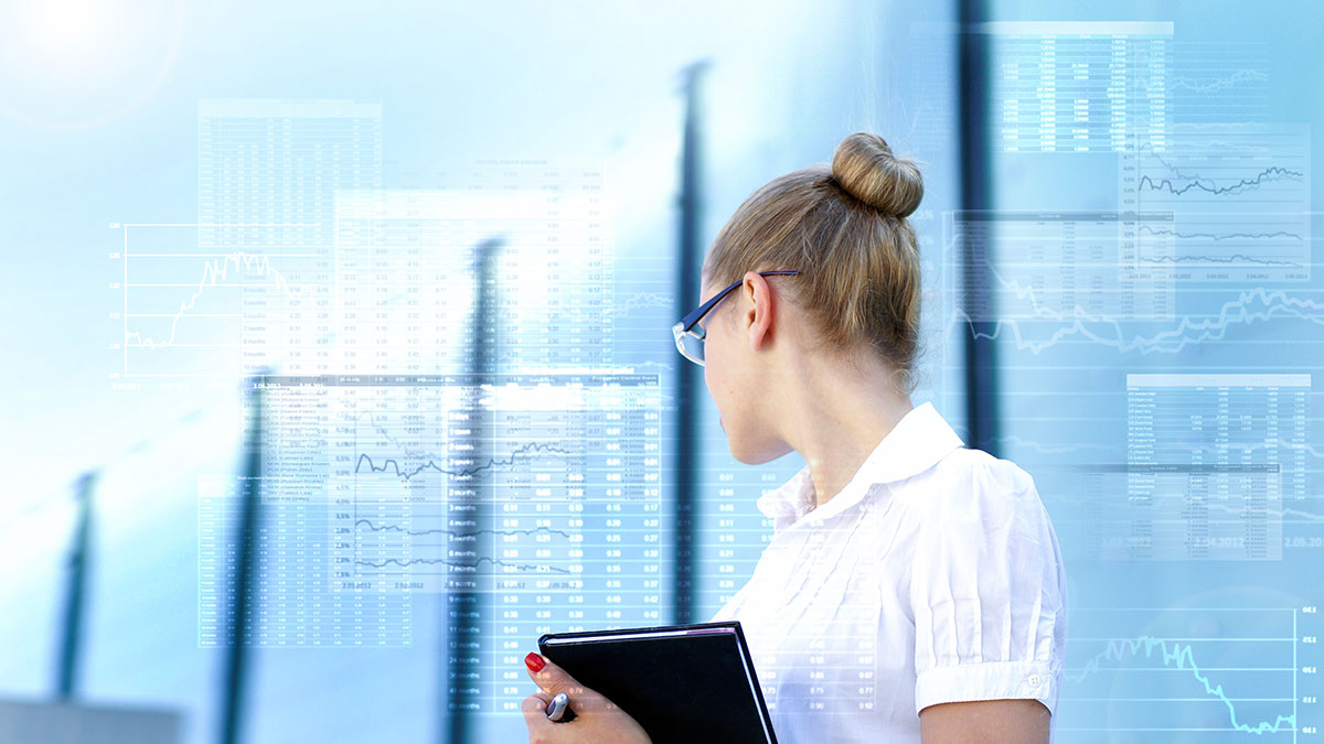 Woman in a white blouse holds a notebook and pen, gazing at superimposed stock charts on a transparent screen. The scene conveys a professional, analytical tone.