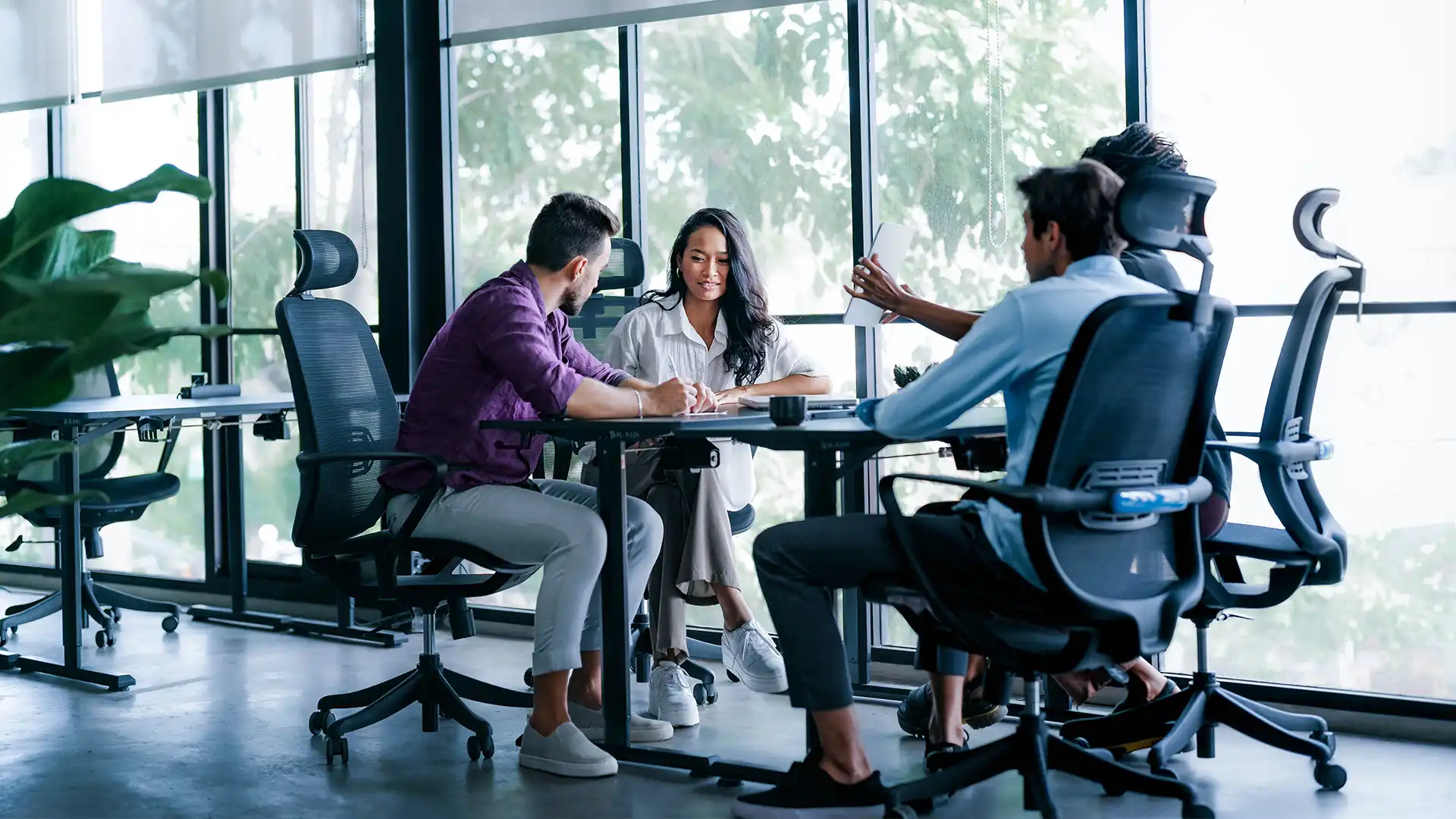 Photo of coworkers sitting around a table in front of a glass walk that looks outside having a discussion