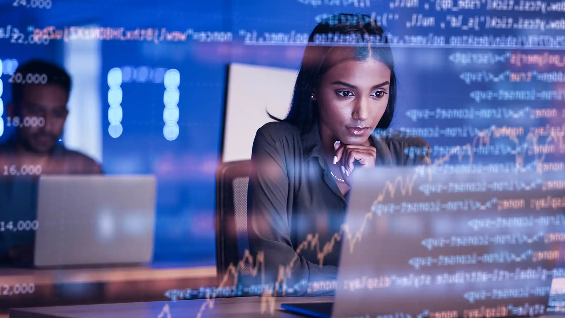 Woman sitting at desk in front of laptop wiht code displayed on screen