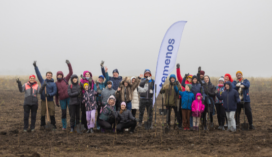 Woman gardening, smiling, in bright outdoor setting. Blue overlay with "temenos" and "Proud to be part of the Mission Earth Team." Earth and leaf icons.